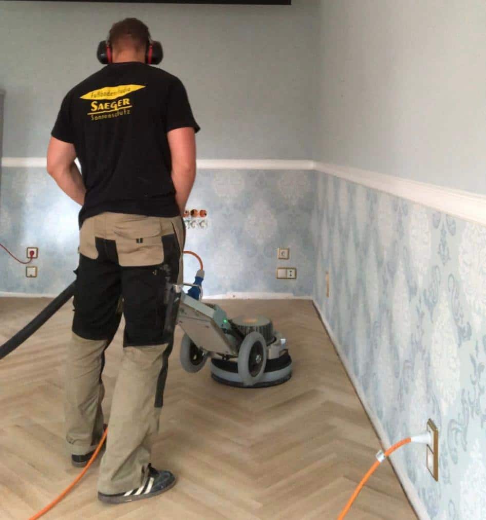 Blog Handwerker beim Parkett schleifen und versiegeln mit Profi-Schleifmaschine in einem Wohnraum.