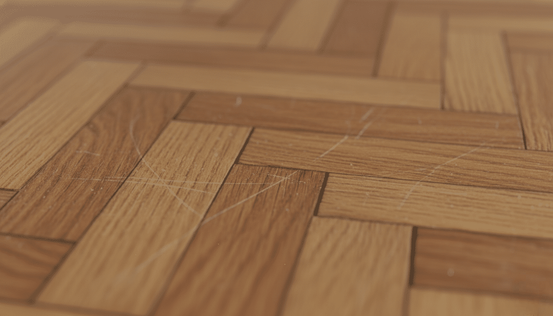 Nahaufnahme eines Parkettbodens mit sichtbaren Kratzern. Erfahren Sie, wie Sie Kratzer im Parkett entfernen und Ihren Boden wieder in Topform bringen können.